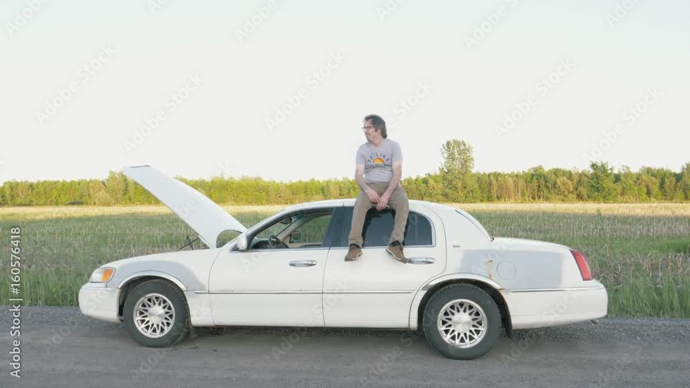Man sitting on top of his car after it broke down in the middle of nowhere. Looking desperate. Man sitting on top of his car after it broke down in the middle of nowhere. Looking desperate.