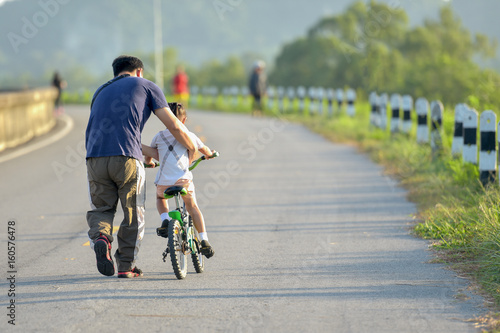 Fototapeta Naklejka Na Ścianę i Meble -  Little kid boy of 3 years and his father in autumn forest with a bicycle. Dad teaching his son. Man happy about success. Child with helmet. Safety sports