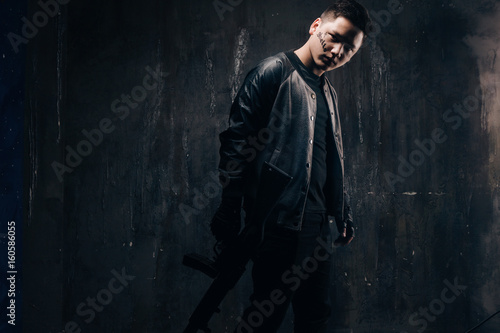 Tattooed killer with sniper rifle in black cloth, studio shoot. Armed white gangster man with weapon and tattoo on dark background with free space. Outlaw, ghetto, murderer, robbery concept