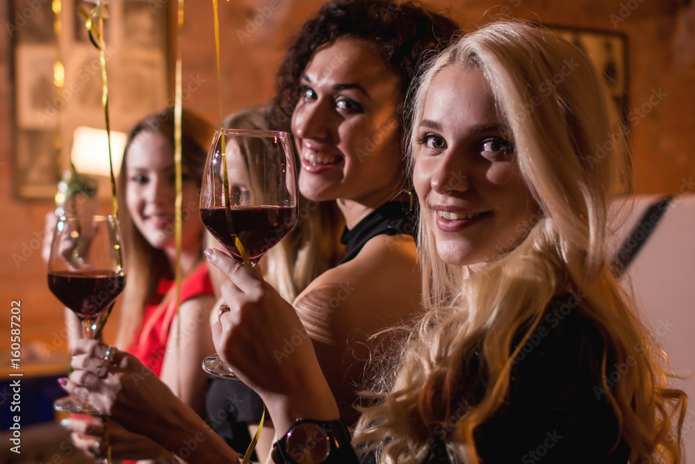 Close-up shot of positive beautiful female friends raising glasses of wine to happy event sitting in fashionable restaurant Close-up shot of positive beautiful female friends raising glasses of wine to happy event sitting in fashionable restaurant