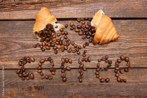 Roasted coffee beans in croissant on wooden background. Closeup of seed filling on dark brown table. Top view. Extra energy concept