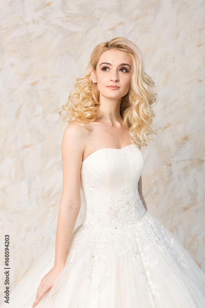 fashionable white gown, beautiful blonde model, bride hairstyle and makeup  concept - young dreaming girl in wedding festive dress, standing indoors on  light background, romantic slender woman posing Stock Photo | Adobe Stock
