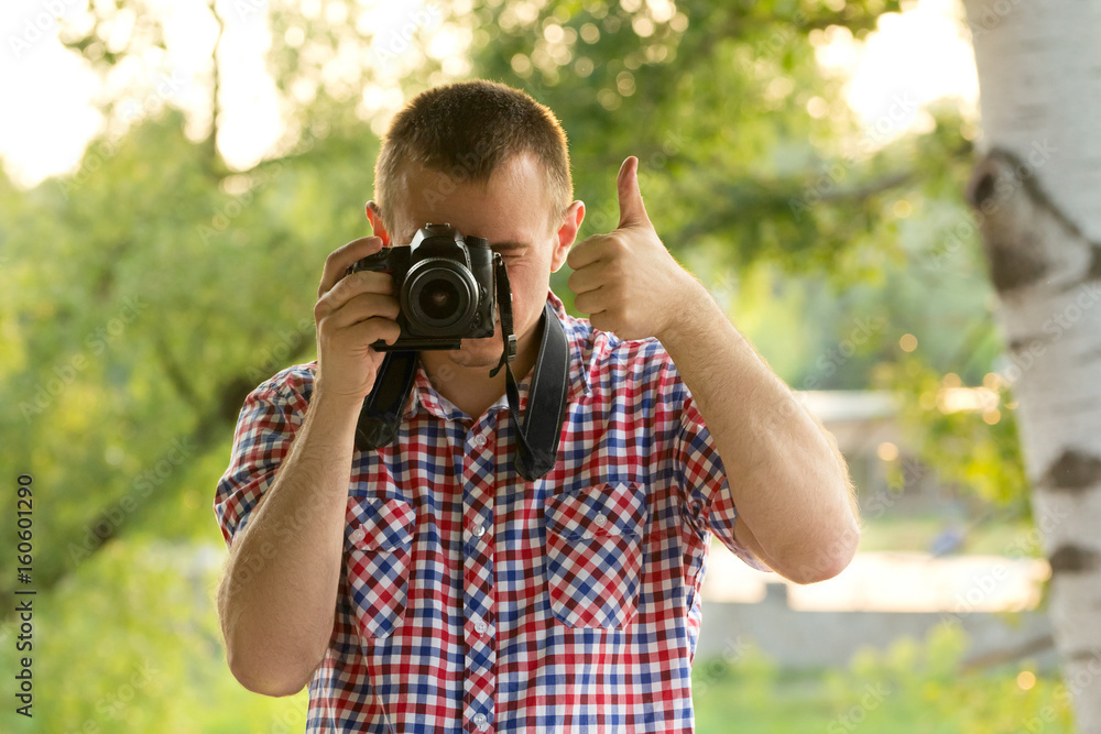 Photographer takes pictures against the background of greenery. Front view. Thumbs up Photographer takes pictures against the background of greenery. Front view. Thumbs up
