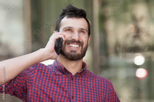 Smiling bearded man doing a phone call. Happy man in modern shirt.