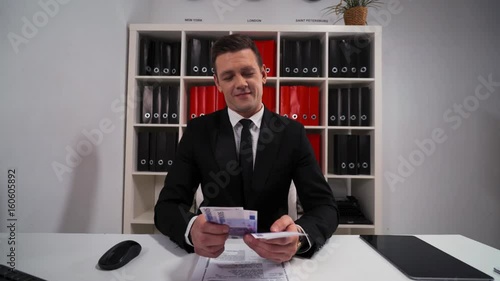 4k uhd POV handsome business man in black suit and tie counting euro with smile. The promise that the work and servise will be done. Hide money in pocket. Office indoor. photo