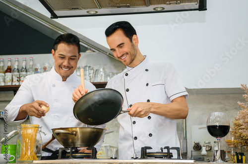 Two young chefs are preparing and cooking food at the kitchen of a restaurant