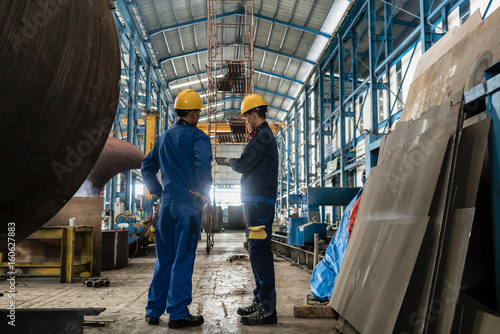 Obraz na plátne Two workers wearing yellow hard hat and blue uniform in the interior of an indus