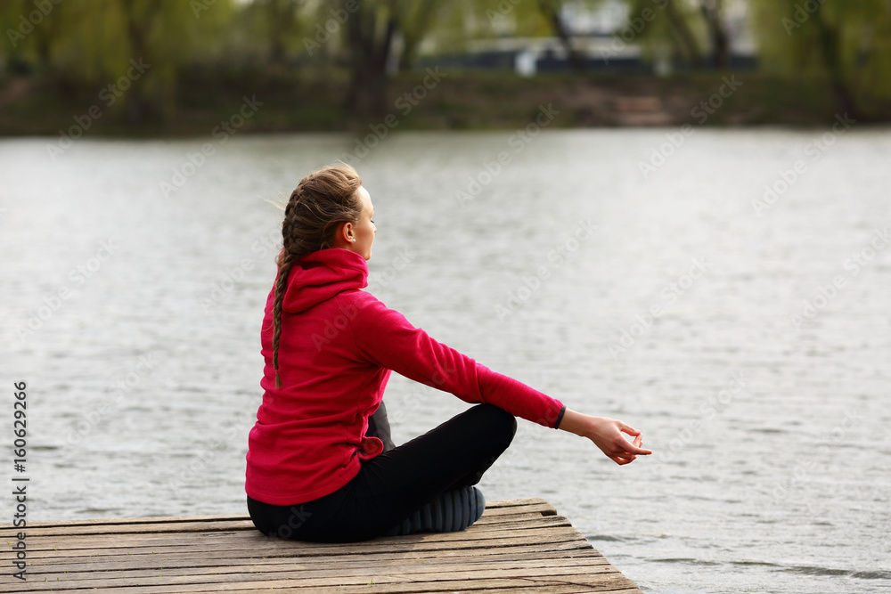 Meditating young woman sitting lotus on pier near water, river,nature, natural background