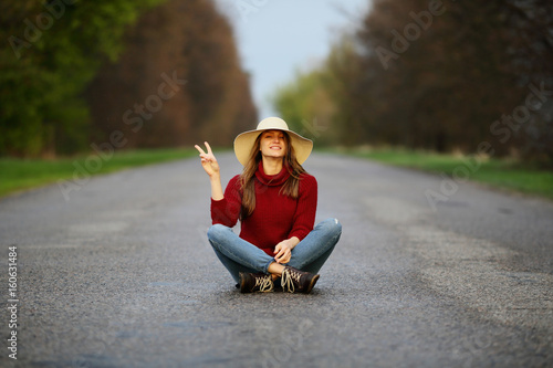 Smiling funny beautiful woman sitting on road, traveling, asphalt, nature