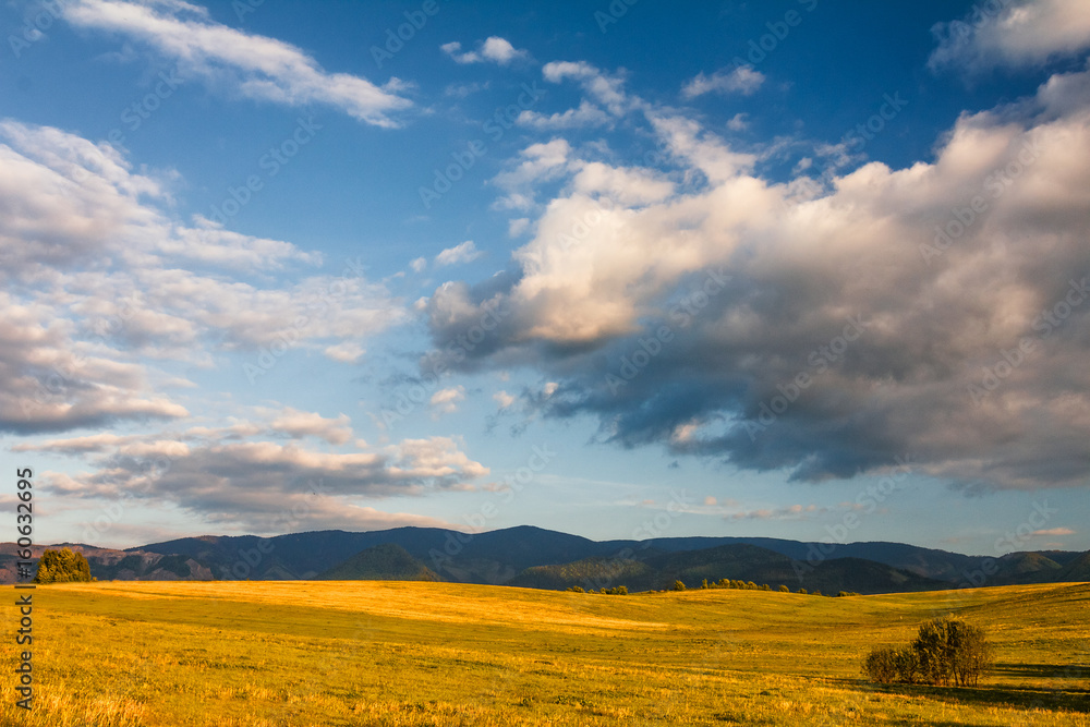 Sunny landscape with mountains and blue sky with clouds in the background.