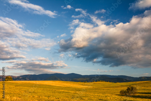 Sunny landscape with mountains and blue sky with clouds in the background.