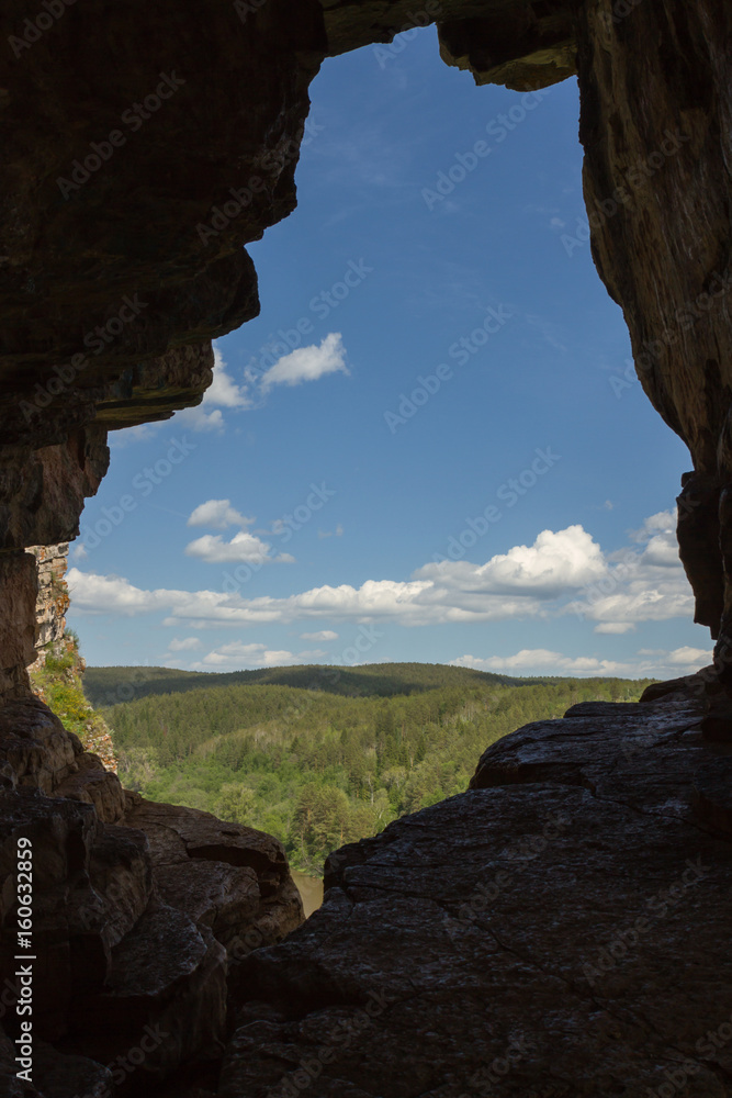 View from the cave of an ancient man on a forest, mountains, sky with clouds.