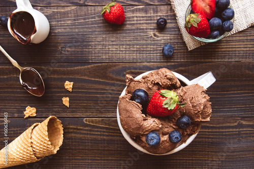 Delicious ice-cream with fresh berries and chocolate sauce on the wooden background, top view