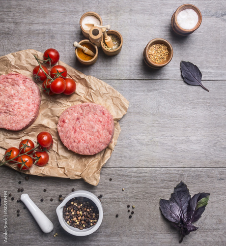 raw cutlet for burgers, with cherry tomatoes and herbs on a packaging paper with unground black pepper, knife for meat on wooden rustic background top view close up place for text,frame