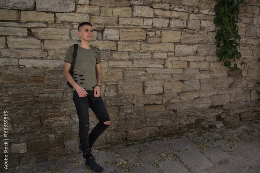 handsome man in glasses standing against a stone wall wearing a black t-shorts looking straight in to camera. handsome man in glasses standing against a stone wall wearing a black t-shorts looking straight in to camera.