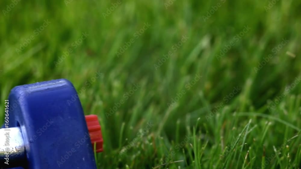 Lawn sprinkler system on garden in grass. Sprinkle sprays water on the green grass in the garden on a background of trees when the sun shines Lawn sprinkler system on garden in grass. Sprinkle sprays water on the green grass in the garden on a background of trees when the sun shines