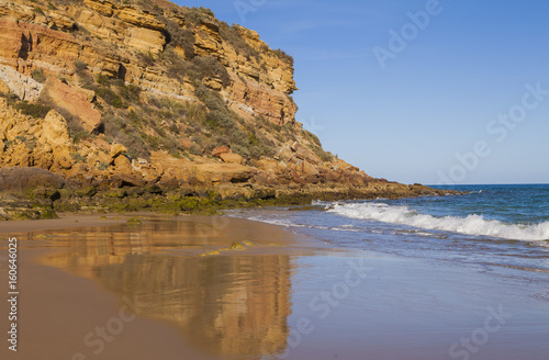Beautiful sandy beach on the coast of Portugal at sunset, the rock is reflected in the wet sand