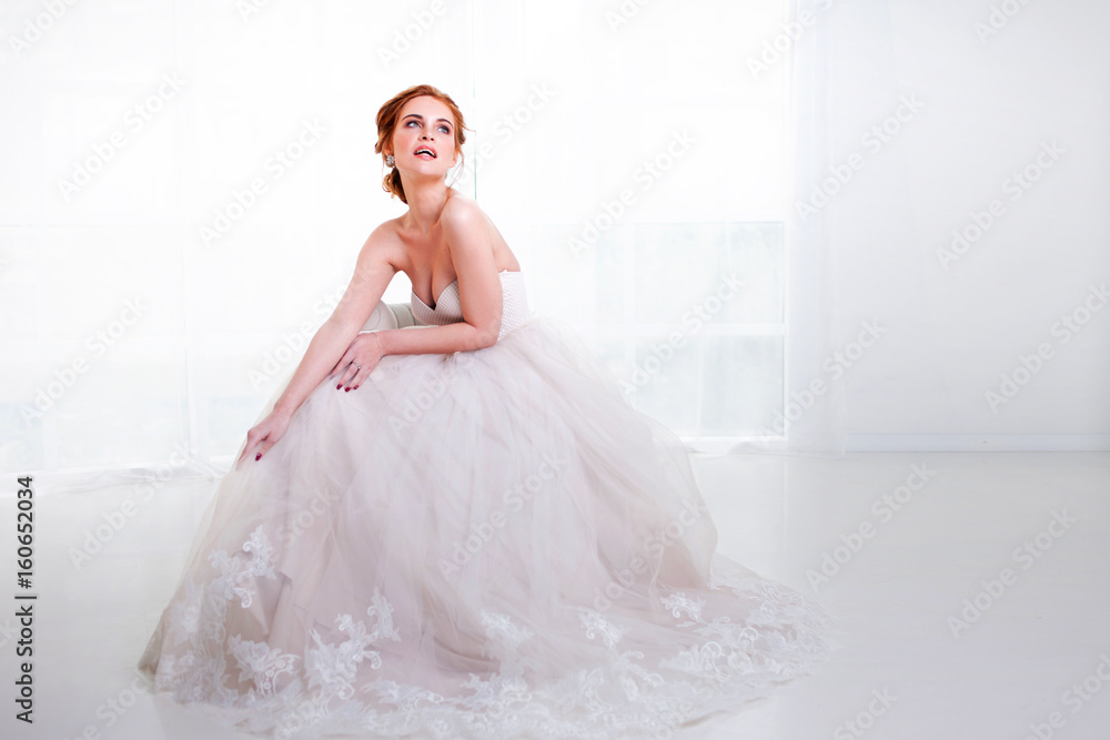 Portrait of a beautiful girl in a wedding dress. Sitting on the couch and laughs happily Portrait of a beautiful girl in a wedding dress. Sitting on the couch and laughs happily