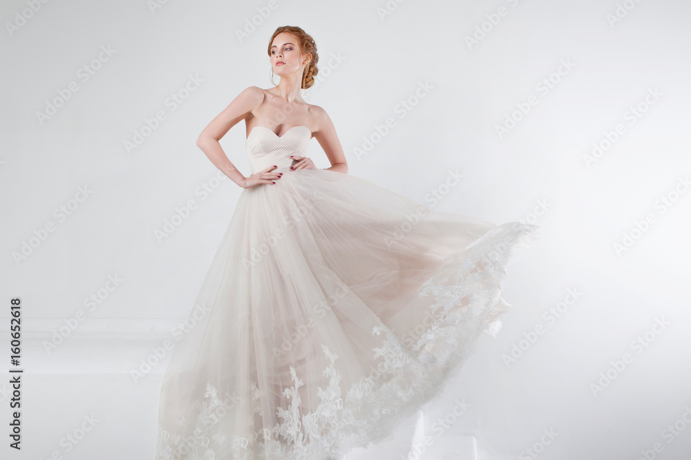 Portrait of a beautiful girl in a wedding dress. Bride in luxurious dress on a white background, hands on waist