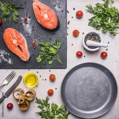 Healthy foods, cooking and sport concept Two fresh salmon steak with herbs and spices on a cutting board stone, laid near cherry tomatoes, whole pepper, pan frying, oil, top view