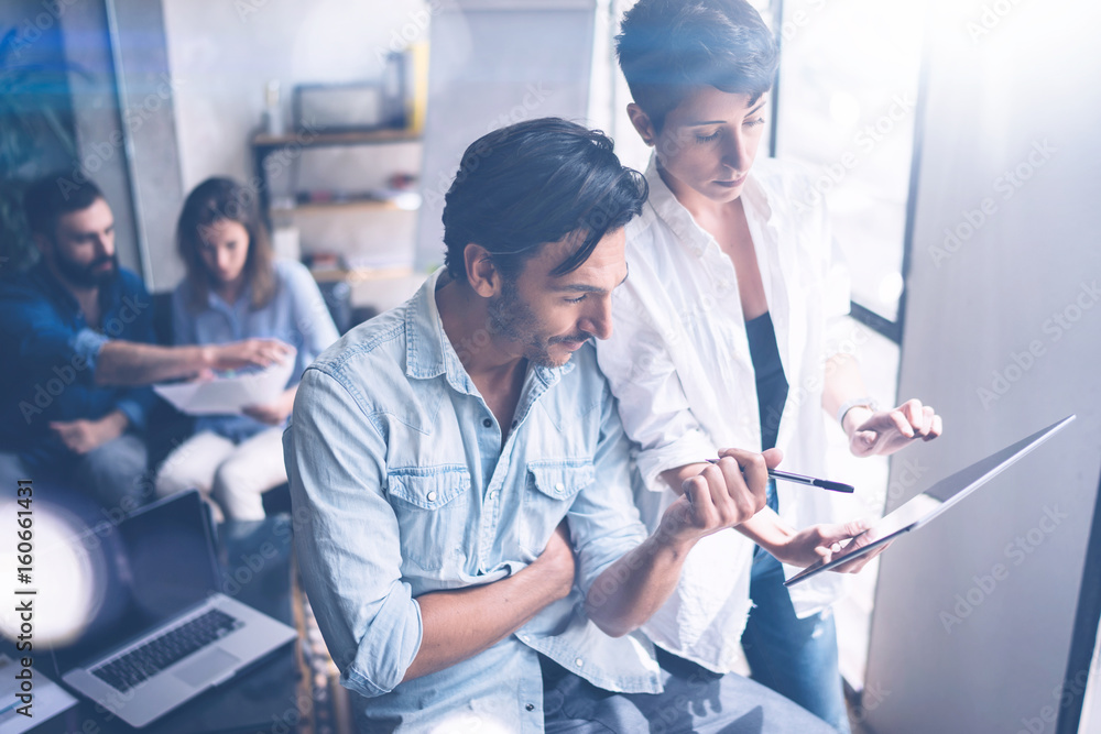 Obraz premium Coworking team meeting.Group of two businessmans working with new startup project in modern office.Touch pad in woman hands. Panoramic windows on blurred background.Flares.