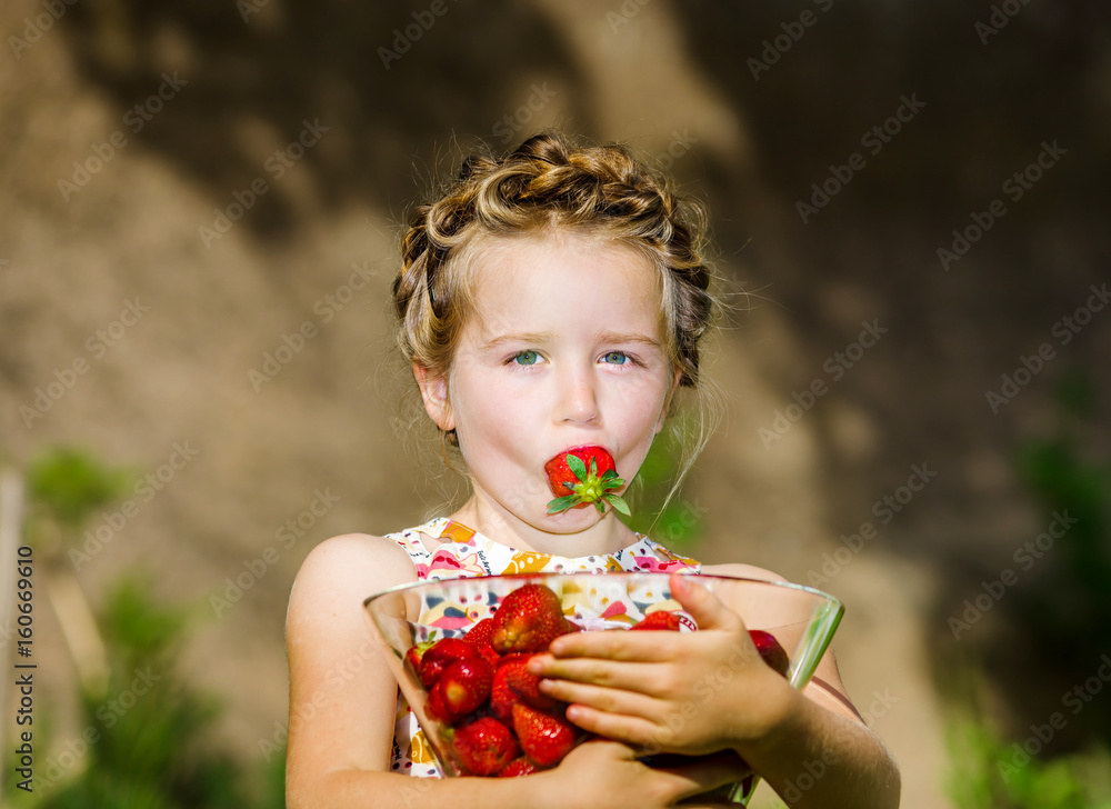Cute little girl posing with fresh red strawberry in the sunny garden Cute little girl posing with fresh red strawberry in the sunny garden