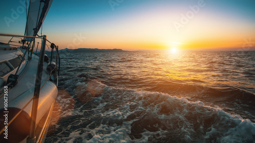 Slide sailing yacht through the waves of the sea during sunset.