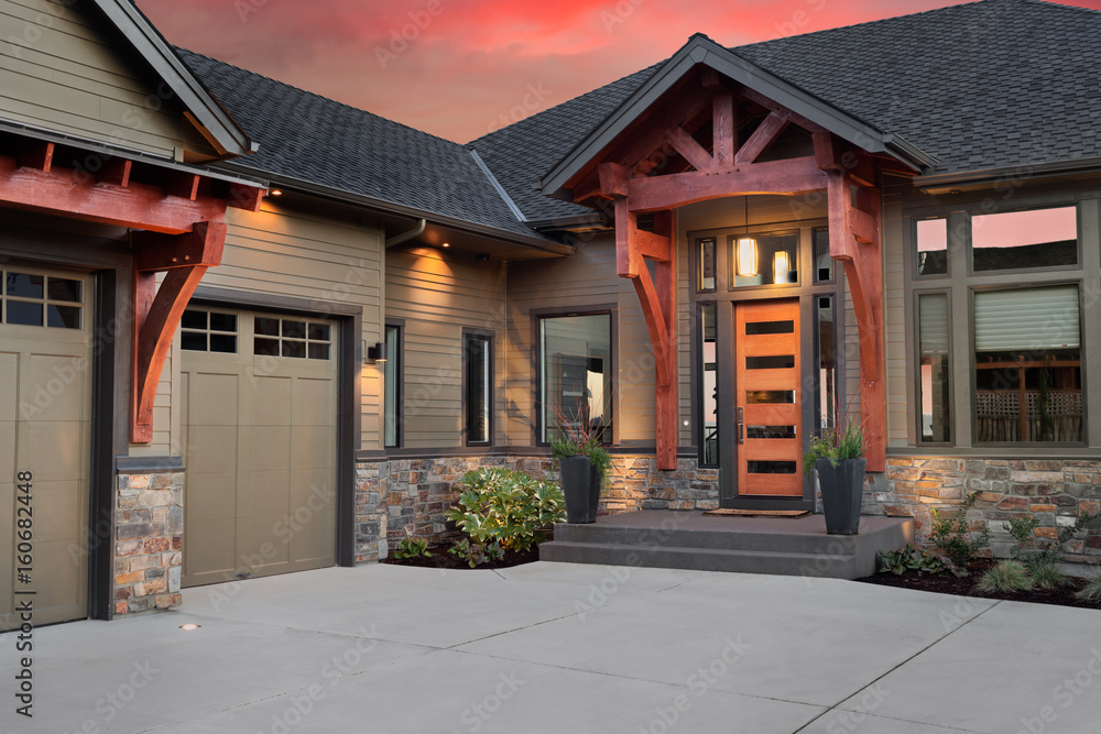 Beautiful Luxury Home Exterior at Sunset: Front Entrance with Elegant Front Door and Partial View of Garage and Driveway. Colorful Sunset Backdrop