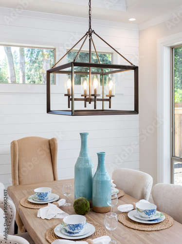 Dining Room Table and Pendant Light Fixture in New Luxury Home. Table is Set with Napkins, Bowls, Plates, and Wine Glasses