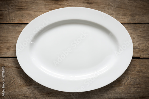 Top view of empty white food plate on a wood background.