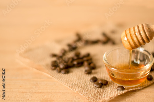 the Honey dipper and fragrant honey into a transparent bowl with coffee bean on wooden background. selective and soft focus at bowl