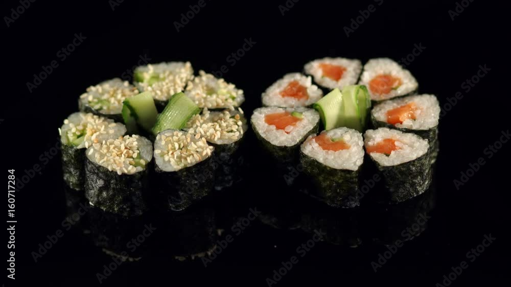 Close-up hand of Japanese chef making sushi, decorating cucumber on black background. The chef decorates cucumber sushi before serving. Close-up hand of Japanese chef making sushi, decorating cucumber on black background. The chef decorates cucumber sushi before serving.