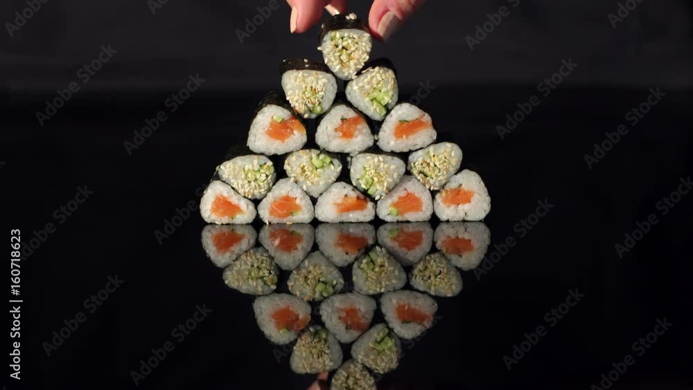 Girl puts sushi on a pyramid on black background, close-up.