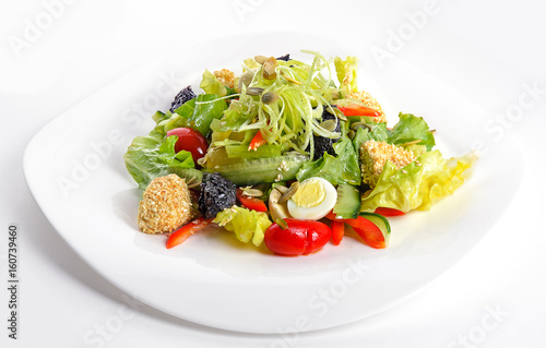 Fresh salad with tapenade, cucumbers, tomatoes and quail eggs on white dish. Isolated on white background. Front view.