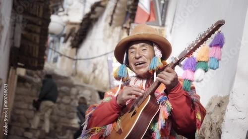 Native quechua man using a colorful handcrafted chullo and a highlander hat, singing with his guitar on the alleys of Cusco photo