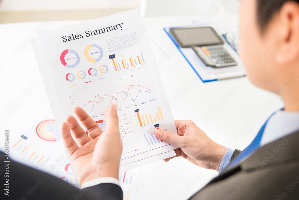 Businessmen discussing and analyzing Sales Summary paper Businessmen discussing and analyzing Sales Summary paper