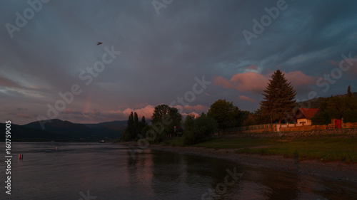 The sun if coming up and more lights by the river with cloudy clouds