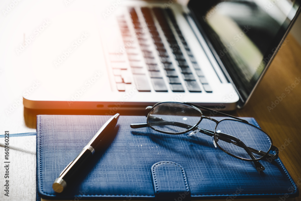Eyeglasses on diary with laptop on wooden table Eyeglasses on diary with laptop on wooden table