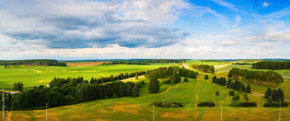Panoramic summer rural landscape. Green fields, meadows, trees, road and blue sky with clouds. Minsk region, Belarus.