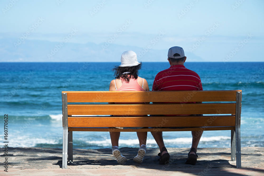 Seniors couple sitting on bench at the beach.Elderly couple looking to the sea