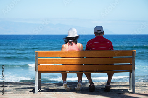 Seniors couple sitting on bench at the beach.Elderly couple looking to the sea