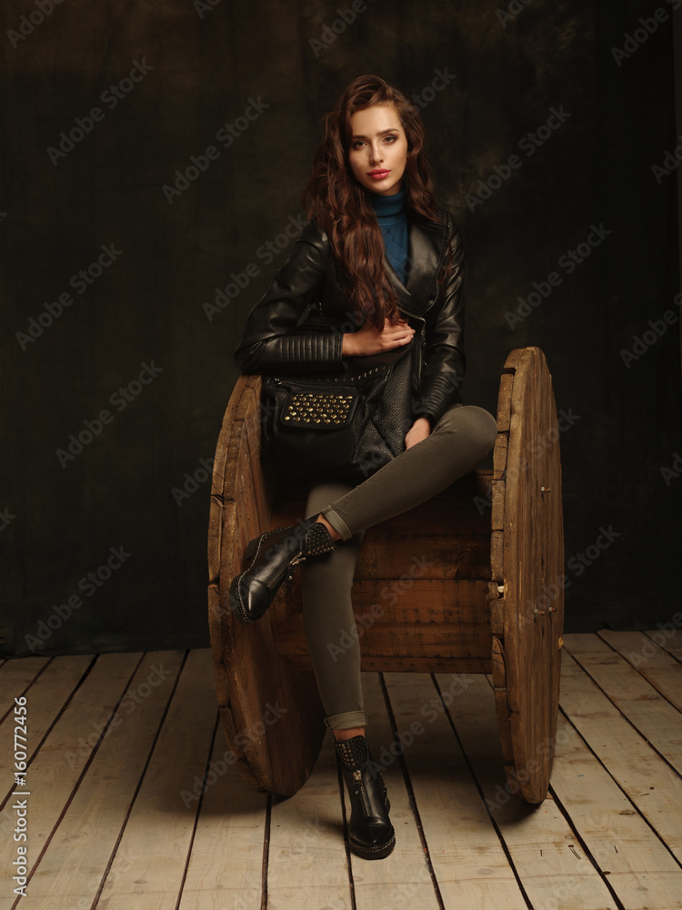 Beautiful, self-contained, confident and successful young woman is posing in a stylish black leather jacket (studio shoot of catalogue of fashionable clothes, model demonstrates the collection) Beautiful, self-contained, confident and successful young woman is posing in a stylish black leather jacket (studio shoot of catalogue of fashionable clothes, model demonstrates the collection)