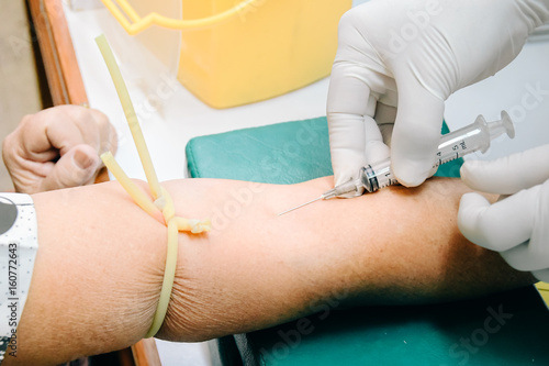 Doctor  hands medical gloves using needle syringe drawing blood sample from patient arm in hospital.