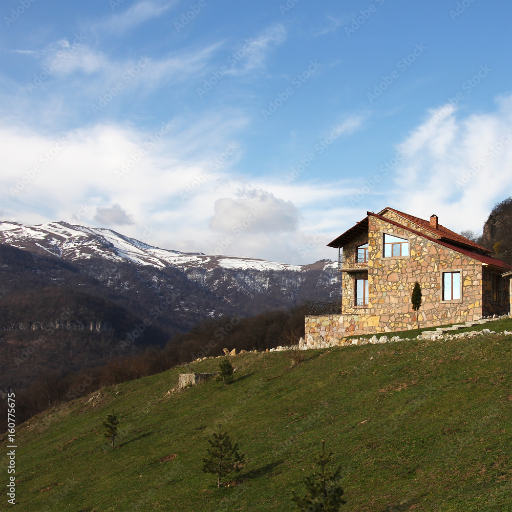 Fototapeta premium lonely stone house on the hill on the background of snowy mountains, square