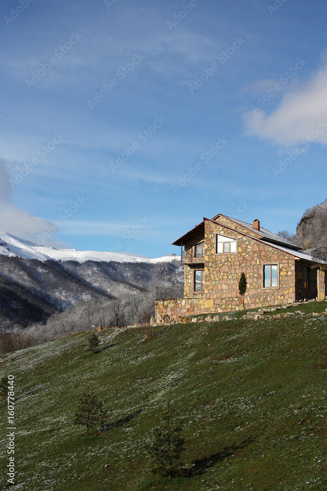 lonely stone house on the hill on the background of snowy mountains, clouds