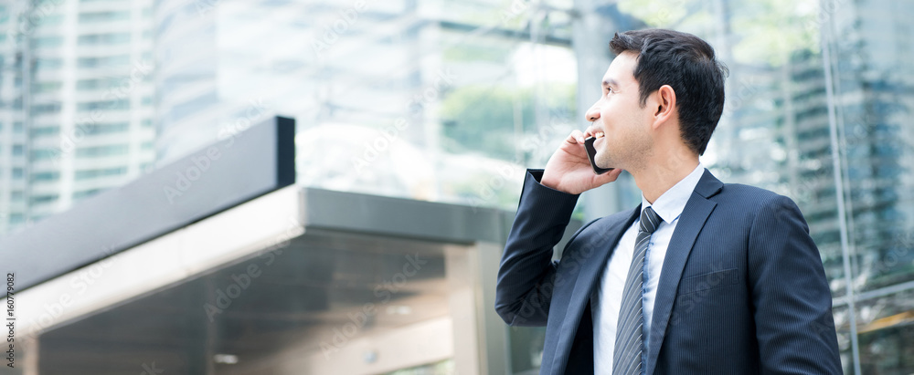 Asian businessman calling on smartphone in front of office building Asian businessman calling on smartphone in front of office building