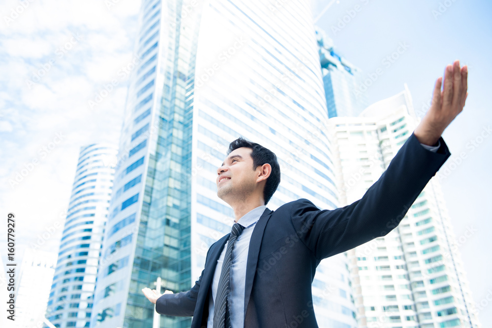 Businessman raising his arms opening palms with face looking up, in office building background Businessman raising his arms opening palms with face looking up, in office building background