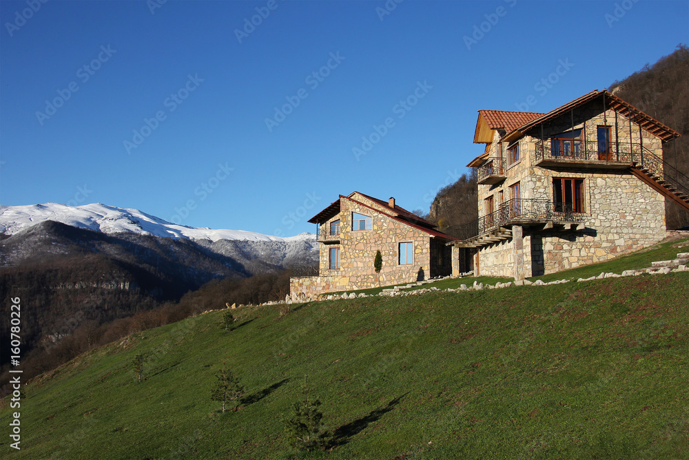 two stone houses on the hill on the background of snowy mountains, clear blue sky, horizontal