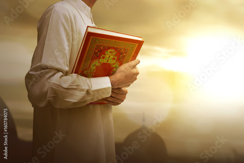 Muslim man in traditional dress holding holy book Koran