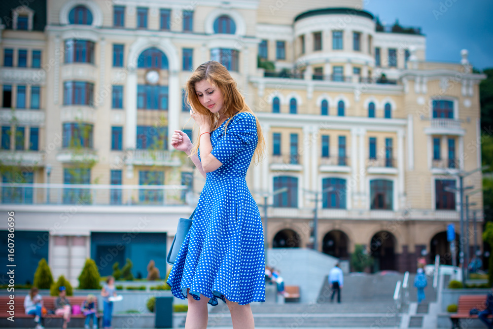 A sweet girl in a blue retro dress is walking in the city and the surrounding area thinking about her life's luck and problems. Vintage in everyday life and style of clothing